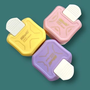 Puede incluir: Tres perforadoras de esquinas de colores amarillo, rosa y morado, cada una con una palanca blanca. Las perforadoras tienen el texto "KW-trio 3-Way Corner Punch". El fondo es de color turquesa.