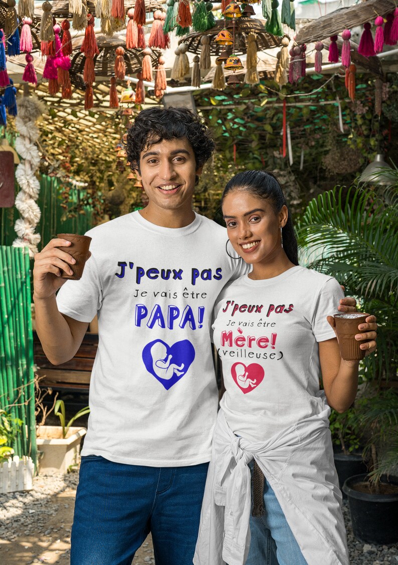May include: A couple wearing white t-shirts with a blue and pink graphic of a fetus inside a heart. The text on the shirts reads "J'peux pas Je vais &ecirc;tre PAPA!" and "J'peux pas Je vais &ecirc;tre M&egrave;re! (veilleuse)".