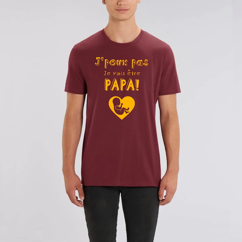 May include: A maroon t-shirt with the text "J'peux pas Je vais &ecirc;tre PAPA!" in yellow with a yellow graphic of a baby in a heart.