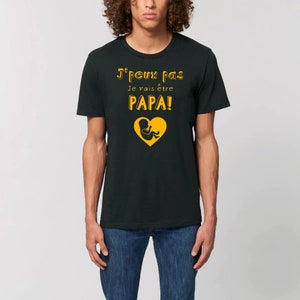 May include: A black t-shirt with the text "J'peux pas Je vais &ecirc;tre PAPA!" in yellow with a yellow silhouette of a baby in a heart.