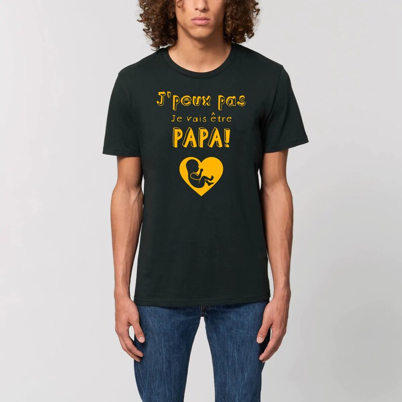 May include: A black t-shirt with the text "J'peux pas Je vais &ecirc;tre PAPA!" in yellow with a yellow silhouette of a baby in a heart.