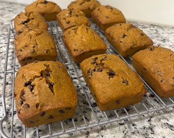May include: A close-up of a cooling rack with ten freshly baked loaves of pumpkin bread with chocolate chips. The loaves are golden brown and have a slightly crispy crust.