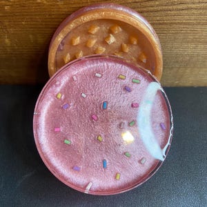 May include: A pink and gold grinder with a sprinkle design. The top of the grinder has a diamond pattern.