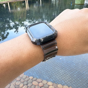 May include: Black Apple Watch with a black metal band and a protective case. The watch is on a person's wrist.