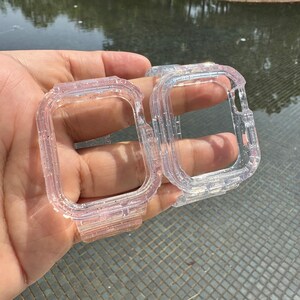Pu&ograve; includere: Due custodie per orologio trasparenti con glitter per un Apple Watch. Le custodie sono in plastica trasparente con una finitura glitterata. Le custodie sono mostrate in una mano.