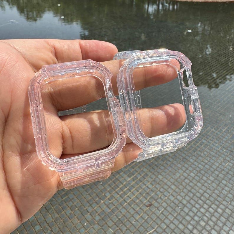 Pu&ograve; includere: Due custodie per orologio trasparenti con glitter per un Apple Watch. Le custodie sono in plastica trasparente con una finitura glitterata. Le custodie sono mostrate in una mano.