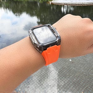 May include: A black and clear protective case for an Apple Watch with an orange silicone band.
