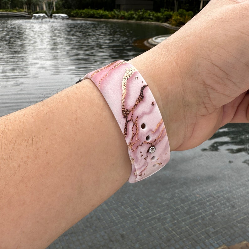 May include: A pink and gold marble patterned watch band with a silver buckle.