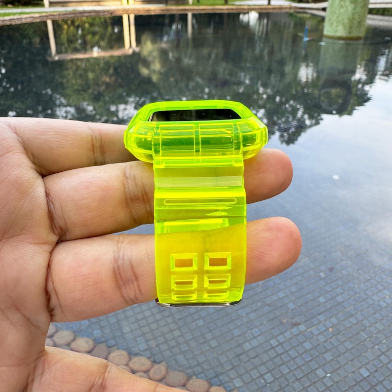 May include: A neon yellow watch case and band. The watch case is rectangular with rounded edges. The band has a series of rectangular cutouts. The watch case and band are made of a translucent material.