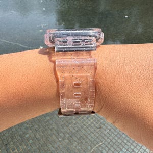 Pu&ograve; includere: Un cinturino per orologio trasparente rosa con glitter incorporati nella plastica. Il cinturino &egrave; progettato per un quadrante dell'orologio quadrato.