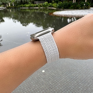 Peut inclure: Un bracelet de montre Apple blanc tressé sur un poignet.