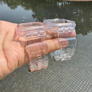Pu&ograve; includere: Due cinturini per orologio trasparenti con finitura scintillante. I cinturini sono realizzati in un materiale flessibile e trasparente e hanno una forma quadrata.