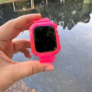 May include: A bright pink clear case for an Apple Watch. The case is made of a flexible, transparent material and has a raised bezel around the screen.