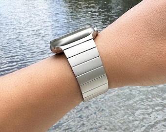 May include: A silver Apple Watch band with a brushed metal finish. The band is made of stainless steel and has a clasp closure.