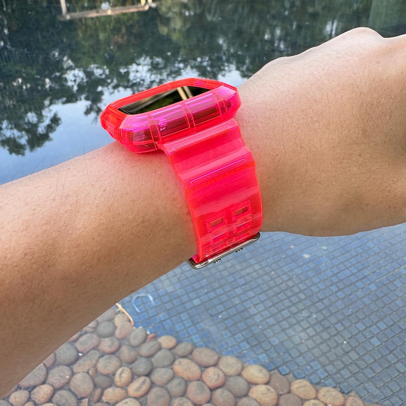 May include: A bright pink clear plastic watch band with a matching case. The band has a grid pattern and is worn on a person's wrist.