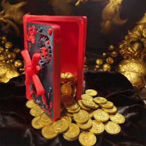 May include: A red and black safe with a red handle and a black door, overflowing with gold coins. The safe is open, revealing the coins spilling out onto a dark surface. The safe door has a decorative design.