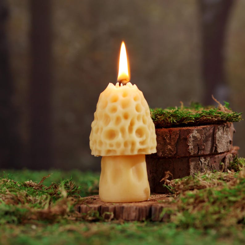 May include: A yellow beeswax candle shaped like a mushroom with a flame burning at the top. The candle is sitting on a wooden base with moss around it.