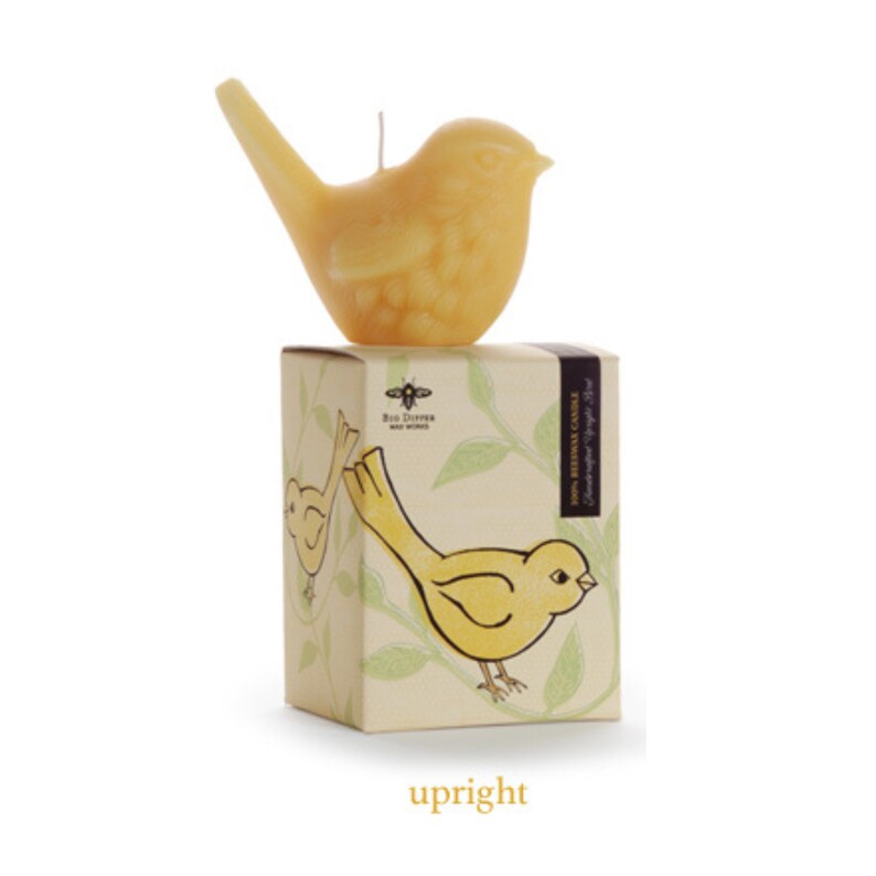 May include: A yellow bird-shaped candle sits on top of a box with a yellow bird illustration. The box is labeled "100% Beeswax Candle" and "Rustic Dreams Hand-Wrought"