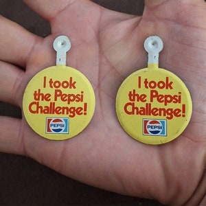 May include: Two yellow round Pepsi Challenge buttons with red and white text. The text on the buttons reads "I took the Pepsi Challenge!" with the Pepsi logo below the text.