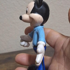 Puede incluir: Una figura vintage de Mickey Mouse. La figura lleva una camisa azul claro, pantalones azules, zapatos negros y guantes blancos. La figura tiene orejas negras y una nariz negra. La figura es de pl&aacute;stico y est&aacute; de perfil.