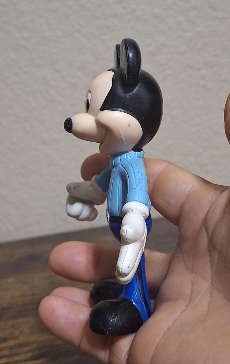 Puede incluir: Una figura vintage de Mickey Mouse. La figura lleva una camisa azul claro, pantalones azules, zapatos negros y guantes blancos. La figura tiene orejas negras y una nariz negra. La figura es de pl&aacute;stico y est&aacute; de perfil.