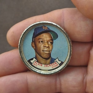 May include: A silver-colored baseball card featuring a portrait of Alvin Jackson, a Mets pitcher. The card has a blue background and a white banner with the text "Alvin Jackson Mets Pitcher".