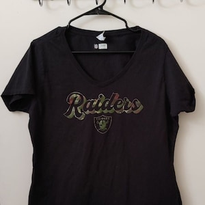 May include: Black t-shirt with a camouflage print of the word "Raiders" and a silver Raiders logo.