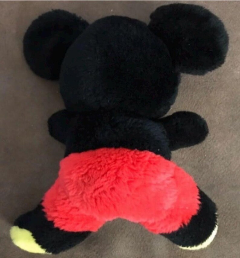 May include: Black and red plush toy shaped like Mickey Mouse. The toy has large ears and a red, fuzzy bottom.