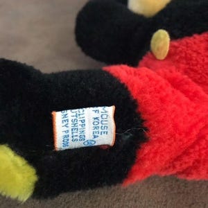 May include: Black and red plush Mickey Mouse toy with a white tag that reads "MOUSE  S. KOREA  FILLINGS  POLYESTER  OUTER SHELL  POLYESTER  DISNEY PROD.  &copy;",