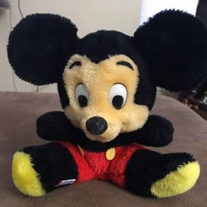 May include: A plush black and yellow Mickey Mouse toy with large black ears and a red and yellow outfit.