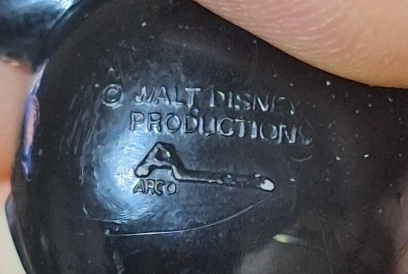 Puede incluir: Primer plano de un objeto de pl&aacute;stico negro con el texto "&copy; WALT DISNEY PRODUCTIONS" y el logotipo "APCO". El objeto parece ser un objeto de colecci&oacute;n vintage, posiblemente un juguete o una figura.