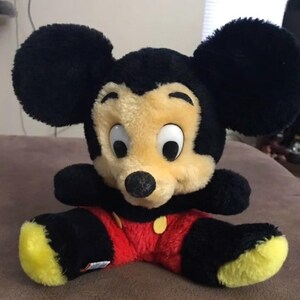 May include: A black and yellow plush Mickey Mouse toy with red shorts and a yellow button. The toy has large black ears and a black nose.