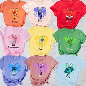 May include: A collection of nine colorful t-shirts, each featuring a different character from the animated movie "Inside Out." The shirts are in various colors, including orange, pink, red, yellow, green, blue, and purple, with character names printed below.