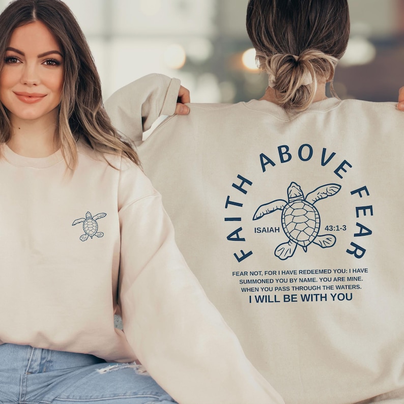 two women wearing matching white sweatshirts with a graphic design and text printed on the back.