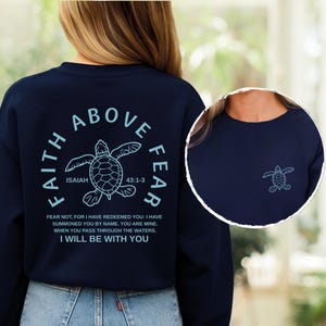 A woman wearing a navy blue sweatshirt with a design featuring a turtle and biblical text.
