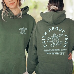 Two women wearing green hooded sweatshirts with a turtle design and text printed on the back.