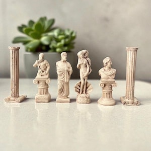 May include: A set of small, off-white classical statues and columns. The statues depict figures such as Poseidon and Venus. The columns and statues are arranged on a white surface, with a succulent plant in the background.