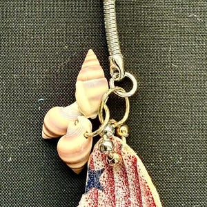 May include: A patriotic keychain featuring a metal ring and a charm with a red and white striped pattern, blue stars, and seashell accents. The keychain is a decorative accessory.