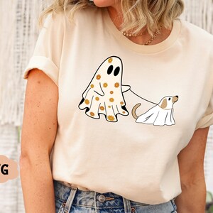 Puede incluir: Una camiseta blanca con un fantasma que lleva un estampado floral y un perro fantasma con una correa.