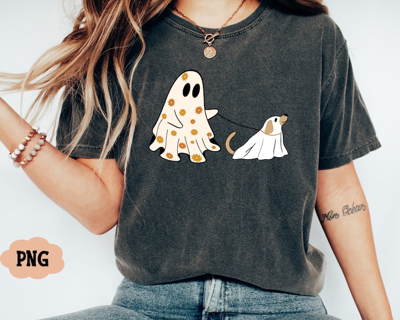 Puede incluir: Una camiseta gris con un gr&aacute;fico de un fantasma que lleva un estampado floral y sostiene una correa atada a un perro fantasma. El texto "More Bean" est&aacute; escrito en la manga derecha de la camiseta.