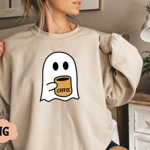 Pu&ograve; includere: Una felpa beige con un fantasma bianco che tiene una tazza di caff&egrave; con la scritta "Coffee".