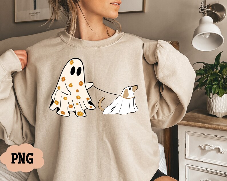 Puede incluir: Una sudadera beige con un estampado gr&aacute;fico de un fantasma con un patr&oacute;n floral y un perro con un disfraz de fantasma. El fantasma sostiene una correa atada al perro.