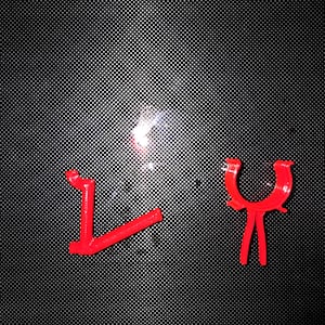 May include: Two bright red plastic components. One piece is L-shaped with a curved end, while the other is a U-shaped clip with two downward-extending legs. Both items feature a smooth, molded finish and are positioned against a dark background.
