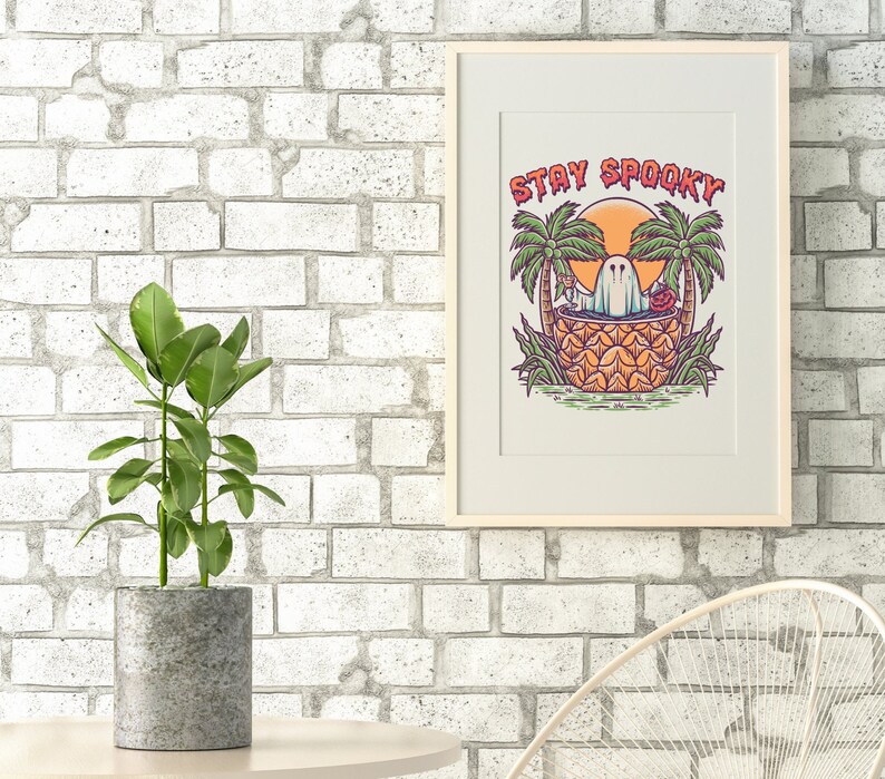 May include: A framed print with a white background and a colorful illustration of a ghost in a pineapple with palm trees and the text "Stay Spooky".