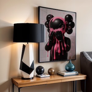 Peut inclure: Intérieur moderne avec une lampe de table géométrique à abat-jour noir et base noire et blanche. Une œuvre encadrée avec une figure noire et des accents roses est accrochée au mur. Sphères décoratives et vase bleu sur une table en bois.