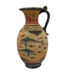 Peut inclure: Une amphore grecque en céramique avec un motif noir et orange représentant deux dauphins nageant parmi des poissons. L'amphore a une anse et un col étroit.