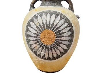 Pode incluir: Um vaso de cerâmica pintado à mão, de cor creme, com um desenho floral preto e prateado. O vaso tem uma borda castanha e duas alças. O centro do desenho floral é um círculo dourado. É um objeto decorativo.