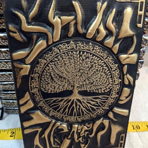 May include: A black leather journal with a gold embossed tree of life design. The journal has a decorative border and a textured surface.