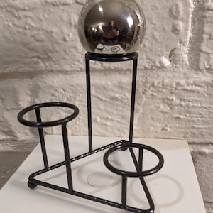 May include: A black metal stand with three circular holders and a single, round, silver-colored orb on top.