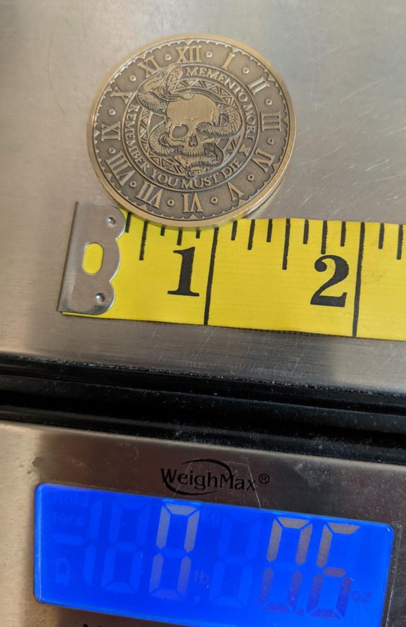 Peut inclure: Une pi&egrave;ce de monnaie en laiton avec un motif de cr&acirc;ne et de serpent. La pi&egrave;ce mesure 1 pouce de diam&egrave;tre et p&egrave;se 16 grammes. La pi&egrave;ce porte l'inscription "Memento Mori" et "Remember You Must Die" sur le bord.